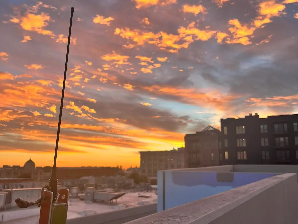 An antenna on a rooftop railing against an orange sunset sky