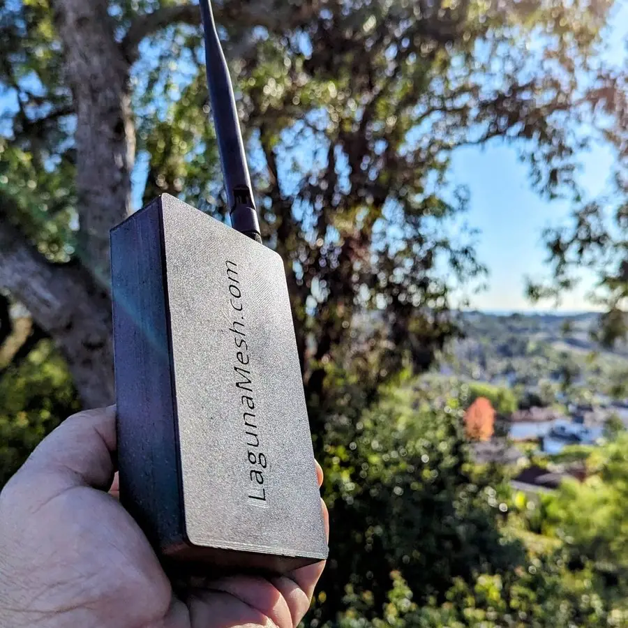 A hand holding a small node in a white case out on a trail
