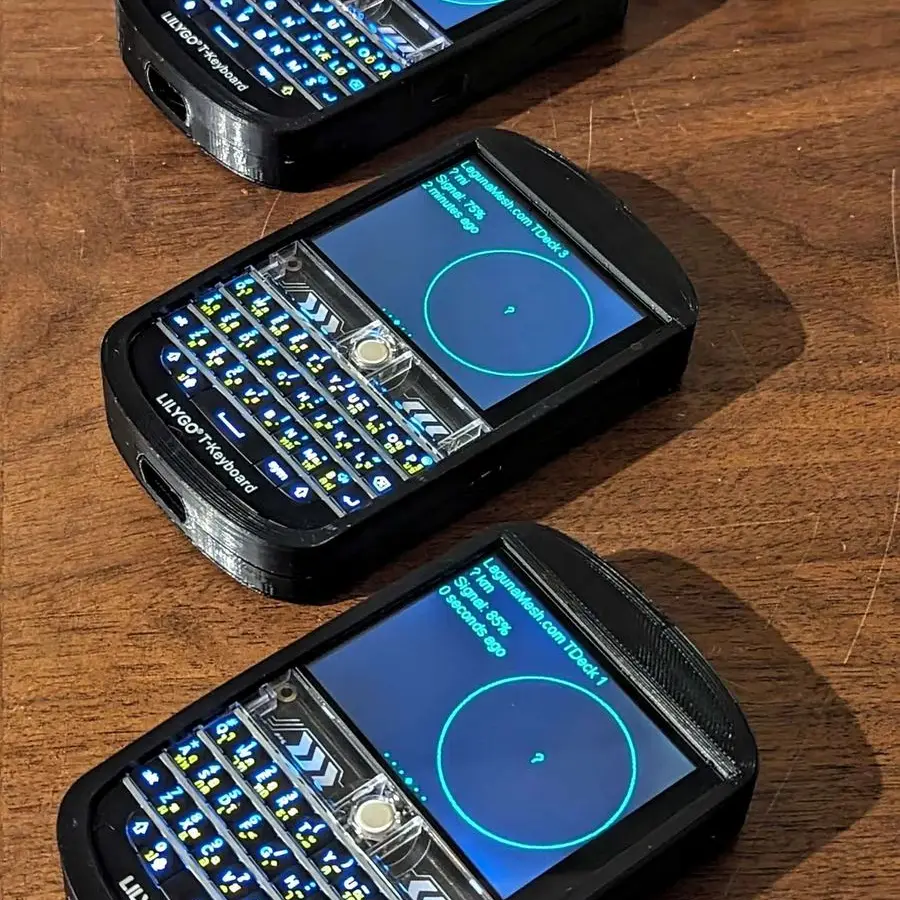 Three handheld radios with keyboards and blue screens laid out on a wooden table
