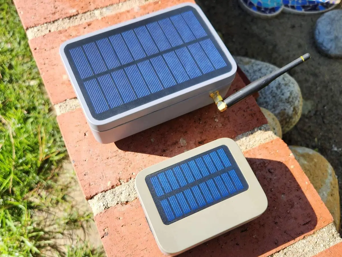 Two solar-powered node enclosures on brick garden edging, panels facing up